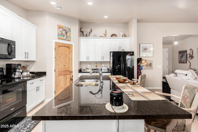 kitchen featuring sink, black appliances, a center island with sink, dark stone countertops, and white cabinets