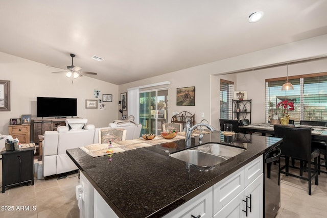 kitchen featuring decorative light fixtures, sink, white cabinets, dark stone counters, and a kitchen island with sink