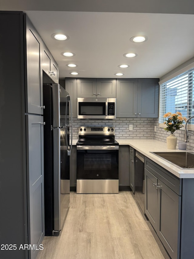 kitchen with a sink, light wood-style floors, gray cabinets, and stainless steel appliances