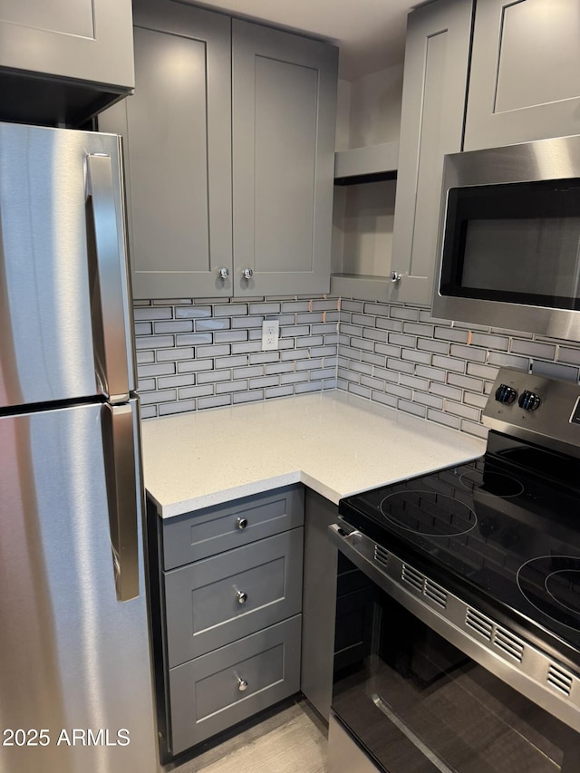 kitchen with decorative backsplash, gray cabinets, appliances with stainless steel finishes, and light wood-style floors