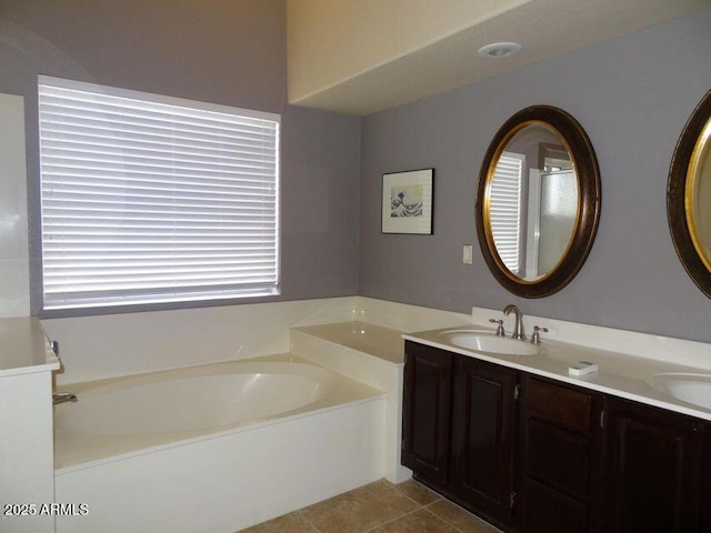 bathroom featuring tile patterned flooring, a garden tub, double vanity, and a sink