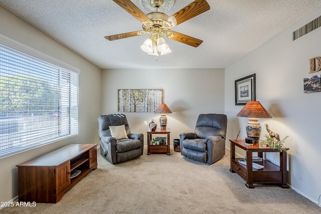 living area featuring ceiling fan, light colored carpet, and a textured ceiling