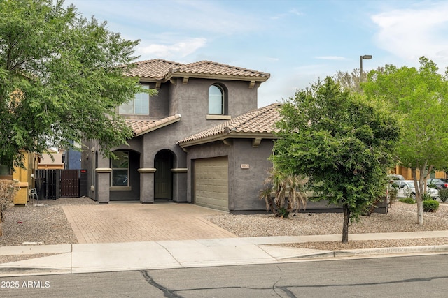 mediterranean / spanish house featuring decorative driveway, a tile roof, a garage, stucco siding, and fence