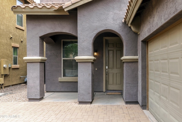 doorway to property with a tiled roof, a garage, and stucco siding
