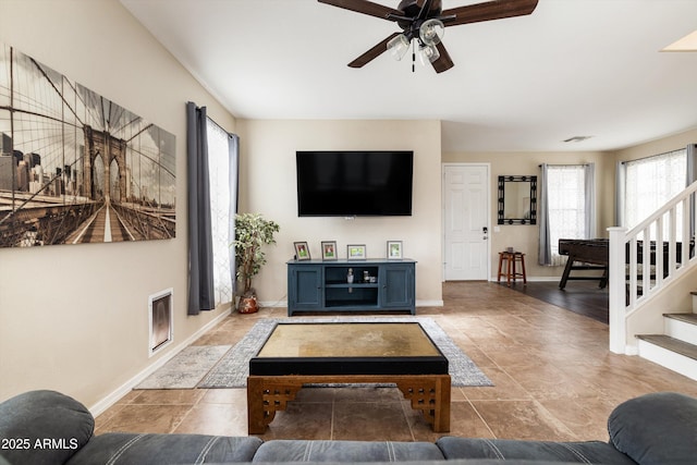 living area featuring ceiling fan, baseboards, and stairs