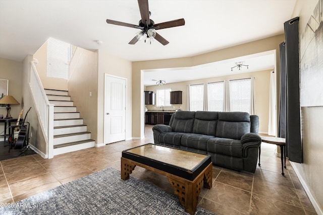 living area featuring baseboards, stairway, a ceiling fan, and tile patterned floors