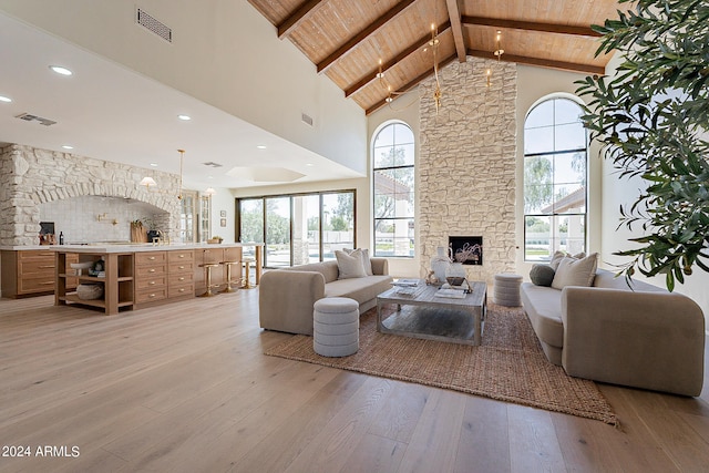 living room featuring a stone fireplace, plenty of natural light, light hardwood / wood-style floors, and wooden ceiling