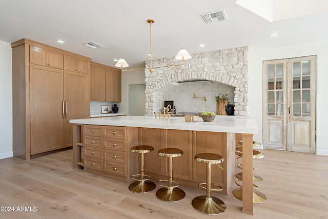 kitchen with tasteful backsplash, decorative light fixtures, a kitchen breakfast bar, a fireplace, and light wood-type flooring