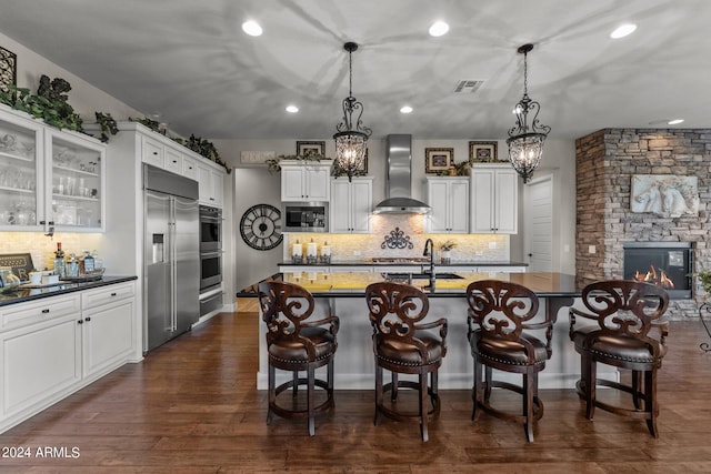 kitchen with pendant lighting, white cabinets, built in appliances, and wall chimney range hood