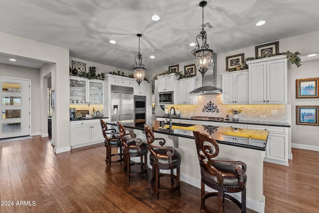 kitchen with white cabinetry, an island with sink, sink, a kitchen bar, and built in appliances