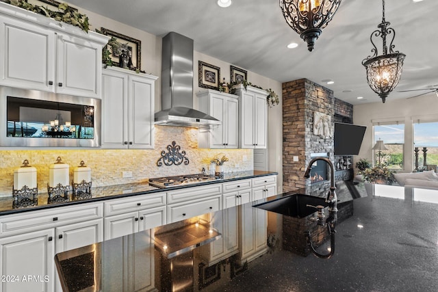 kitchen with appliances with stainless steel finishes, pendant lighting, sink, white cabinets, and wall chimney exhaust hood