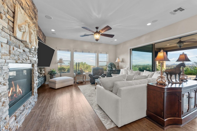 living room with ceiling fan, a stone fireplace, and hardwood / wood-style floors