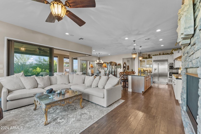 living room featuring dark wood-type flooring, ceiling fan with notable chandelier, and sink