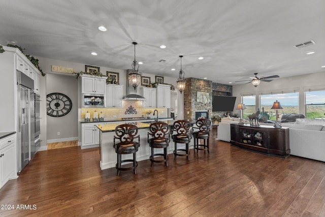 kitchen featuring pendant lighting, a kitchen breakfast bar, white cabinets, a center island with sink, and dark hardwood / wood-style flooring