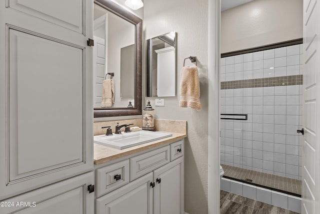 bathroom featuring hardwood / wood-style flooring, tiled shower, vanity, and toilet