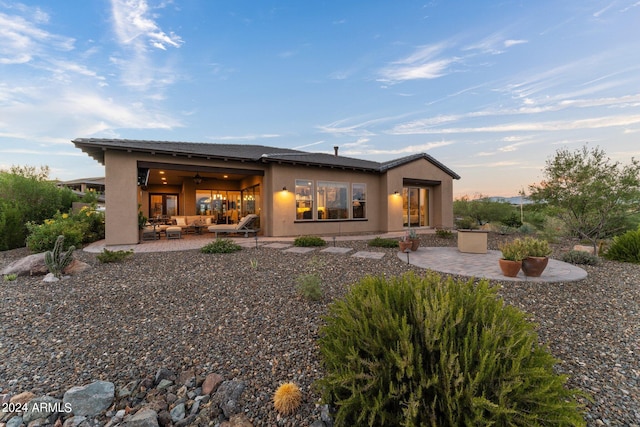 back house at dusk with outdoor lounge area and a patio