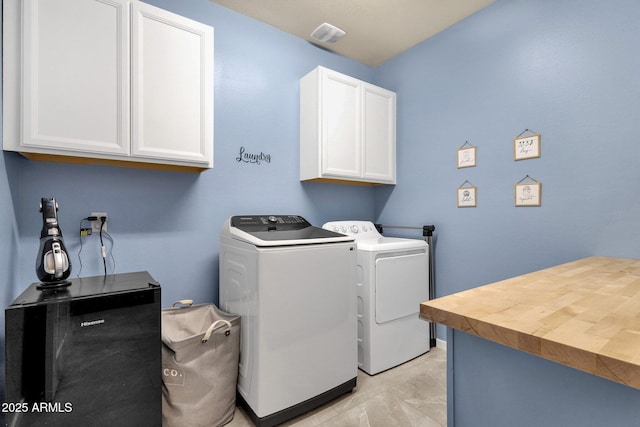 clothes washing area featuring cabinets, light tile patterned flooring, and washing machine and clothes dryer