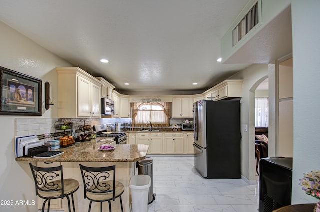 kitchen with sink, backsplash, a kitchen breakfast bar, stainless steel appliances, and kitchen peninsula