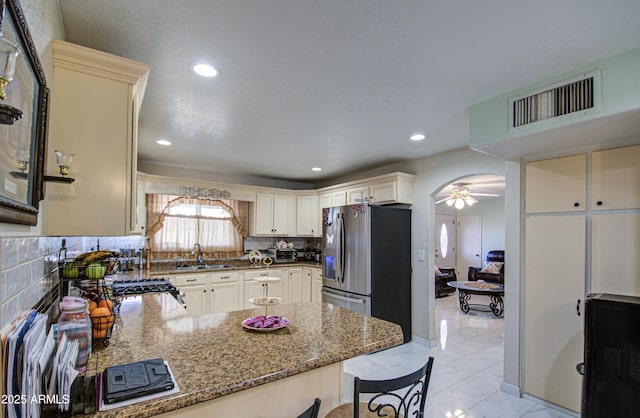 kitchen with sink, stainless steel fridge, decorative backsplash, dark stone counters, and kitchen peninsula