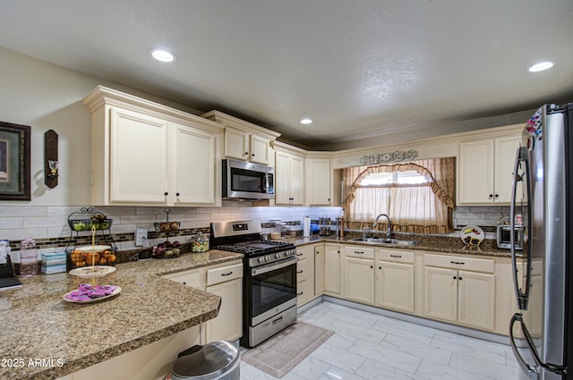 kitchen with sink, stone countertops, appliances with stainless steel finishes, decorative backsplash, and cream cabinetry