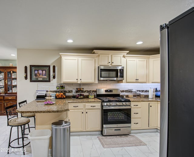 kitchen featuring tasteful backsplash, stainless steel appliances, a kitchen breakfast bar, and cream cabinetry