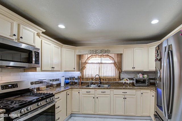 kitchen with appliances with stainless steel finishes, sink, backsplash, dark stone counters, and cream cabinets