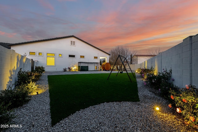 back house at dusk featuring a yard and a playground