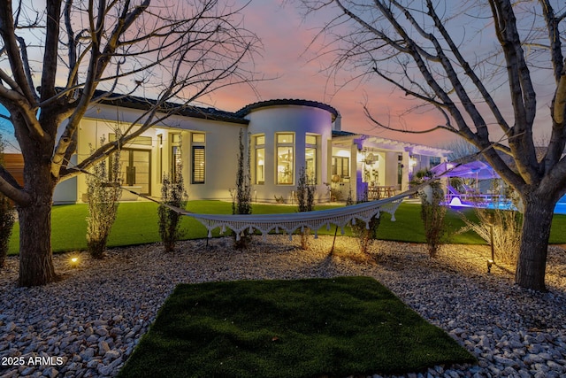 back house at dusk with a lawn