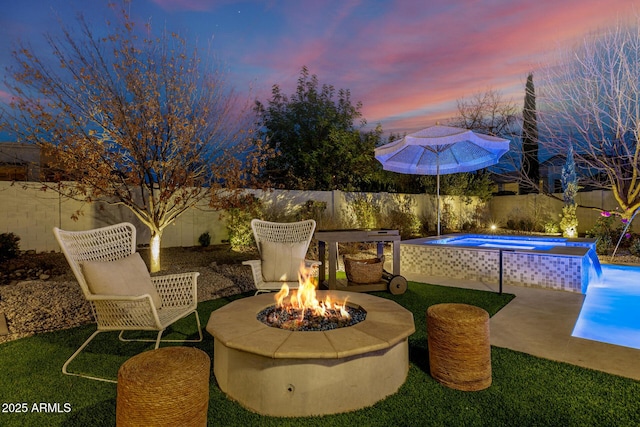 patio terrace at dusk featuring a fenced in pool, pool water feature, and an outdoor fire pit