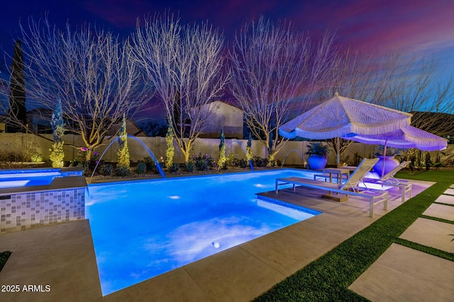 pool at dusk with a jacuzzi, pool water feature, and a patio area