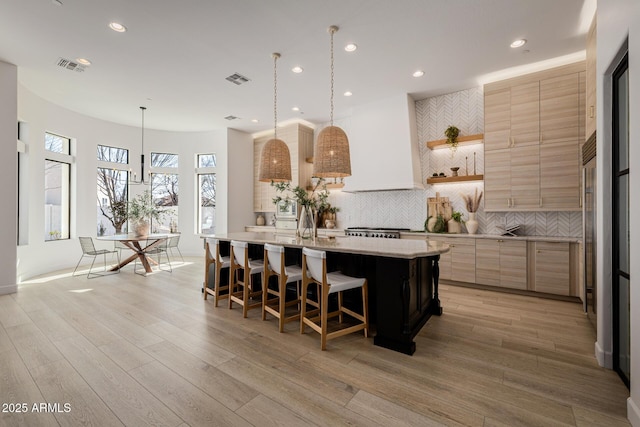 kitchen featuring a center island with sink, decorative light fixtures, tasteful backsplash, custom range hood, and a kitchen breakfast bar