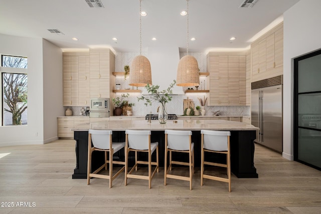 kitchen featuring built in appliances, a kitchen breakfast bar, pendant lighting, and a kitchen island with sink