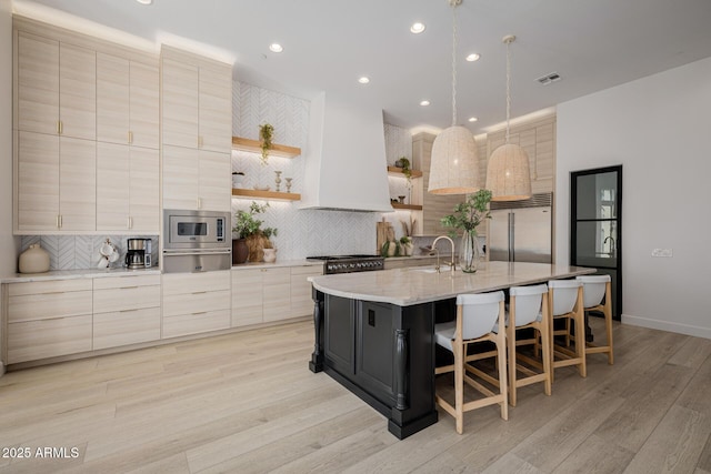 kitchen featuring built in appliances, a kitchen breakfast bar, custom range hood, sink, and a kitchen island with sink