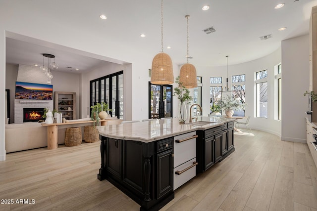 kitchen featuring light hardwood / wood-style flooring, pendant lighting, a large island, and light stone counters