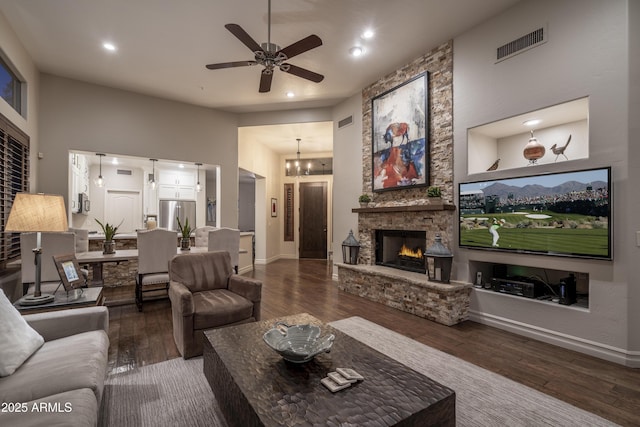 living room featuring a high ceiling, dark wood-type flooring, ceiling fan with notable chandelier, and a fireplace