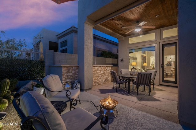 patio terrace at dusk with ceiling fan and an outdoor living space with a fire pit