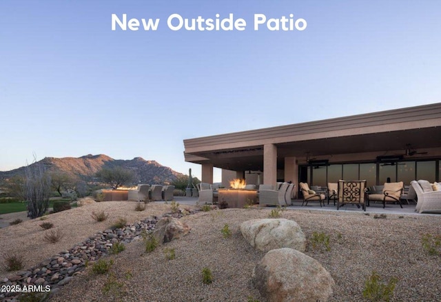 rear view of property featuring a mountain view, a patio area, an outdoor living space with a fire pit, and ceiling fan