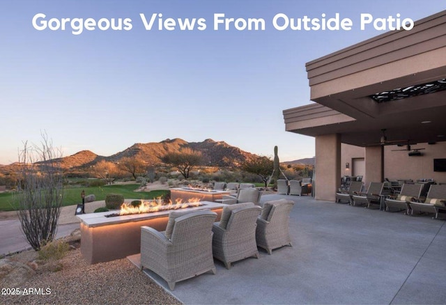 view of patio featuring a mountain view, ceiling fan, and an outdoor fire pit