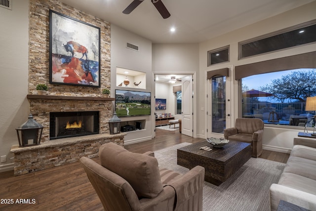 living room with ceiling fan, a fireplace, hardwood / wood-style floors, and a towering ceiling