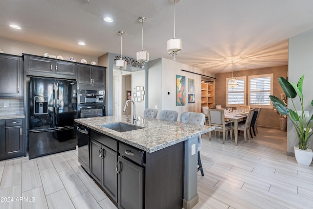 kitchen with a breakfast bar, sink, black appliances, a center island with sink, and hanging light fixtures