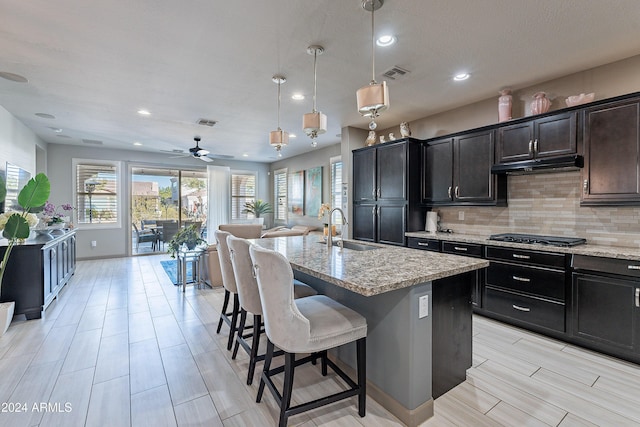 kitchen featuring decorative light fixtures, light stone counters, a kitchen island with sink, and sink