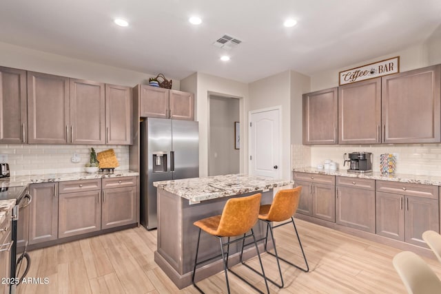 139 E Gail Dr, Gilbert, AZ 85296 - kitchen featuring stainless steel fridge with ice dispenser, electric stove, decorative backsplash, light wood finished floors, and light stone counters