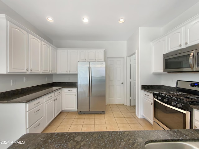 kitchen with white cabinets, light tile patterned floors, stainless steel appliances, and dark stone counters