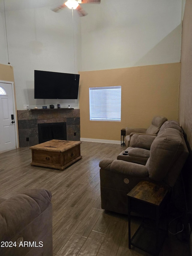 living room with a tile fireplace, hardwood / wood-style flooring, ceiling fan, and a towering ceiling