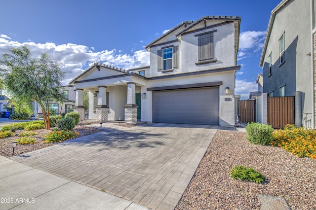 view of front facade with covered porch, fence, a garage, stucco siding, and decorative driveway
