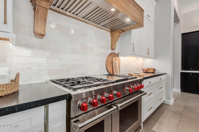 kitchen with custom exhaust hood, range with two ovens, white cabinetry, and backsplash