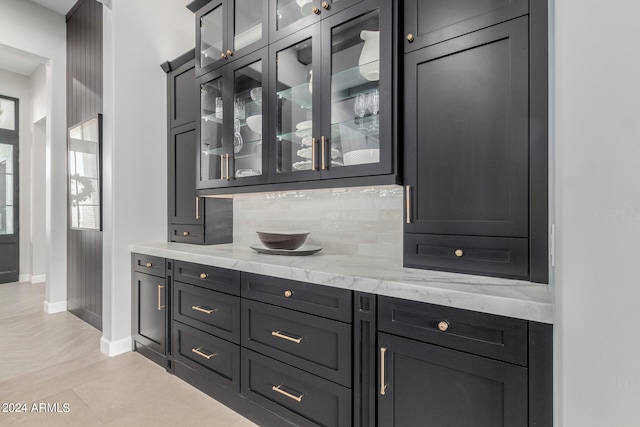 bar with tasteful backsplash, light stone countertops, and light tile patterned floors