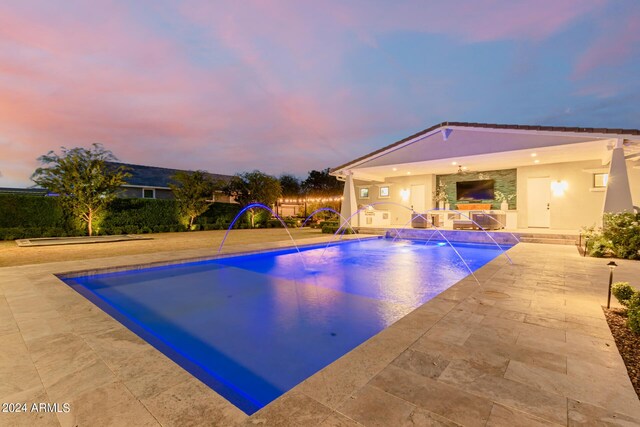 pool at dusk featuring pool water feature and a patio