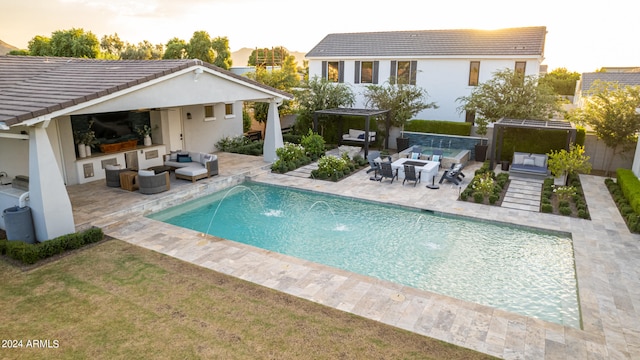 back house at dusk with pool water feature, an outdoor kitchen, a patio, and an outdoor hangout area