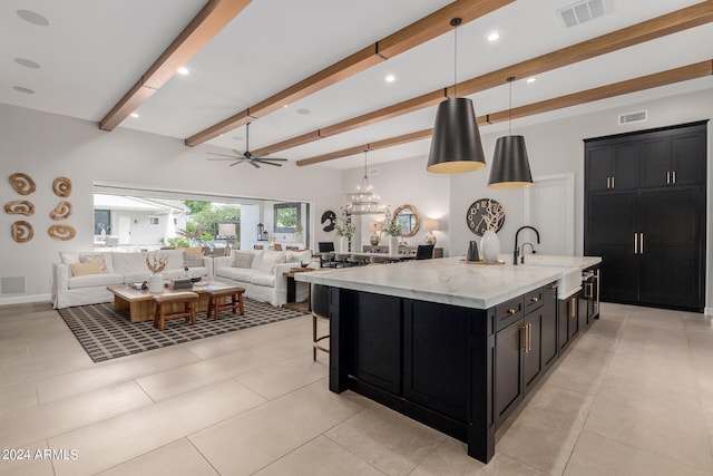 kitchen featuring beam ceiling, a large island, hanging light fixtures, light stone counters, and ceiling fan with notable chandelier